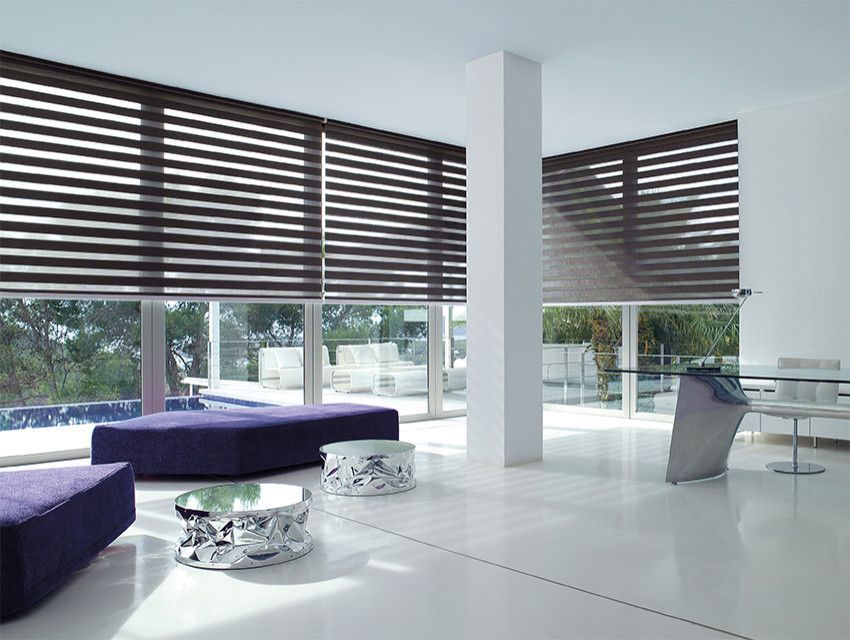 Modern living room with large windows, dark blinds, white floors, and purple sofas