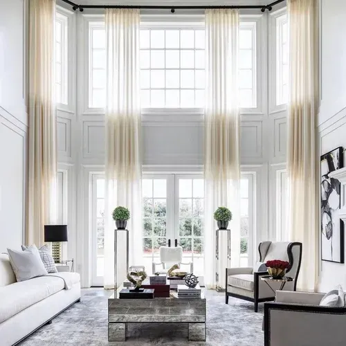 Bright white living room with tall windows, sheer curtains, a sofa, chairs, and a coffee table