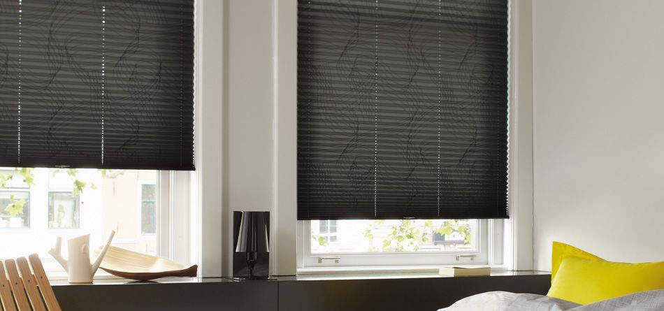 Windows with black blinds in a bright room, with a small table and yellow cushion near the window.