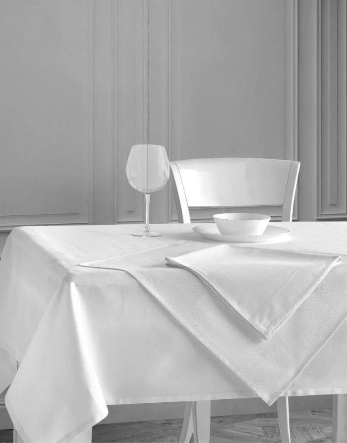 Set dining table with white tablecloth, wine glass, bowl, and chair in a bright room