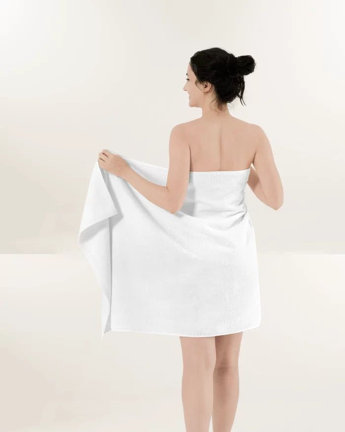 Woman wrapped in a white towel, standing and looking over her shoulder in a bright studio