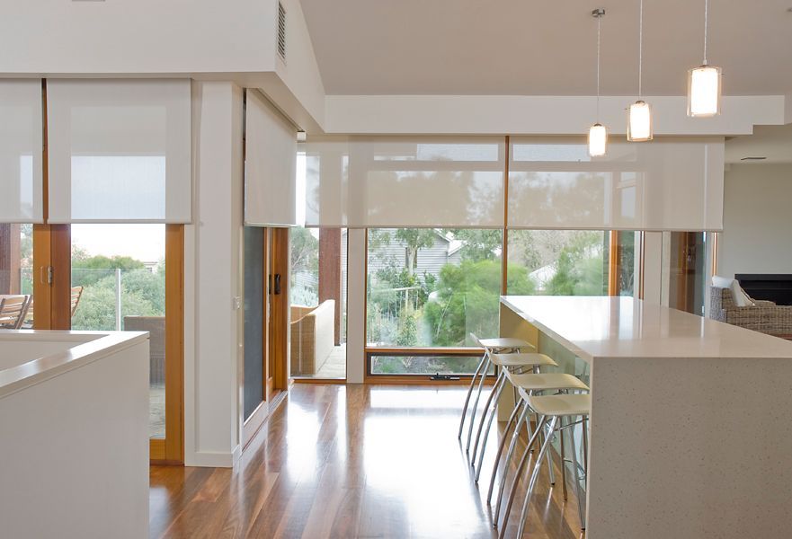 Modern kitchen and dining area with barstools, pendant lights, and large windows overlooking greenery