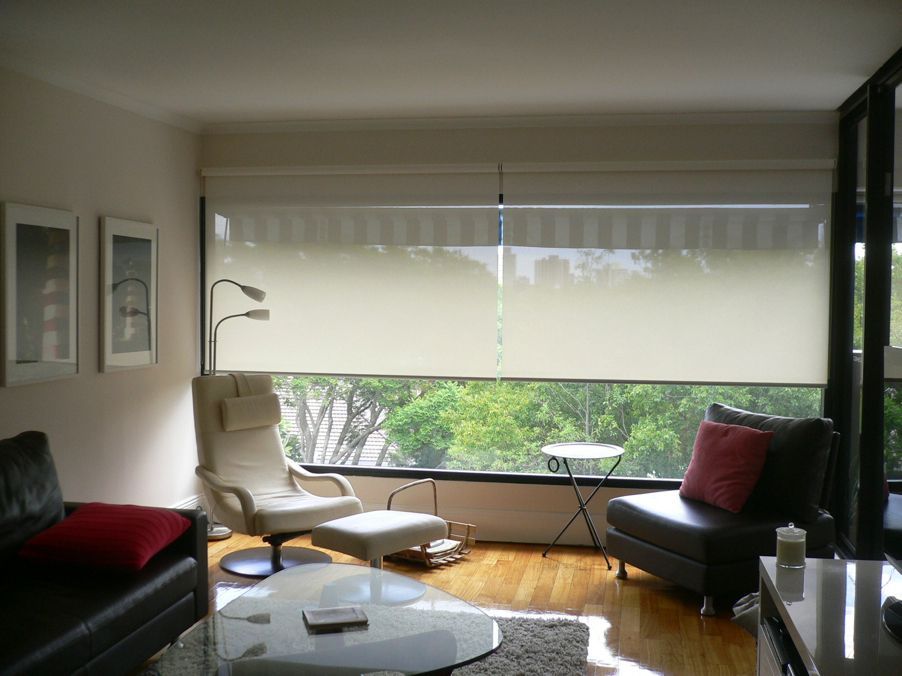 Modern living room with white blinds, black sofas, red cushions, and a glass coffee table.