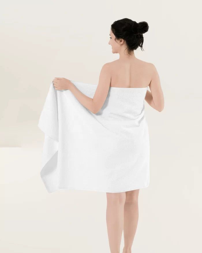 Person in a white towel, standing with back turned against a plain light background.