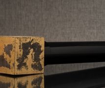 Close-up of a worn yellow-and-black painted block beside a glossy black cylinder on a reflective surface