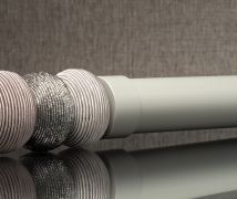 Gray corrugated hose with woven metallic sleeve beside a white pipe on a reflective surface