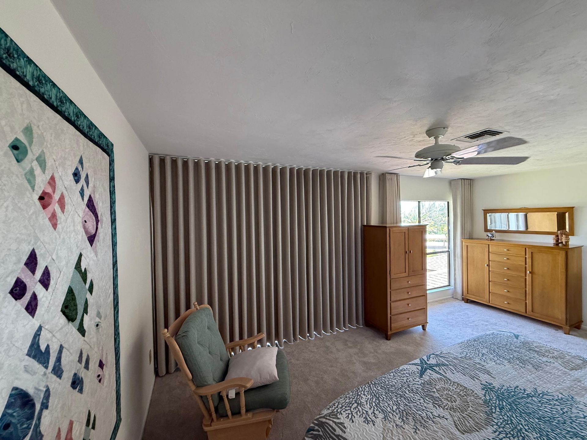 Spacious bedroom with striped curtains, wooden dresser, chair, and blue patterned rug near a window.