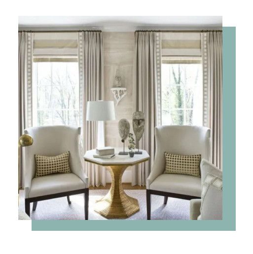Elegant sitting area with two upholstered chairs, round pedestal table, lamp, and large windows with curtains