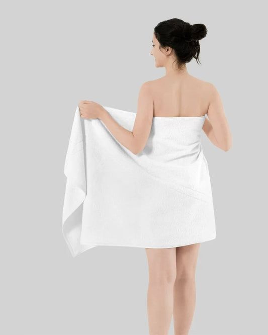 Woman wrapped in a white towel, seen from behind against a light gray background