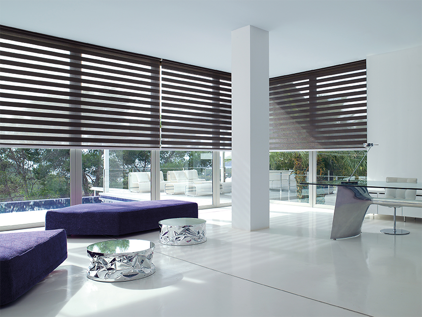 Modern living room with purple sectional sofa, glass tables, and large windows with dark blinds