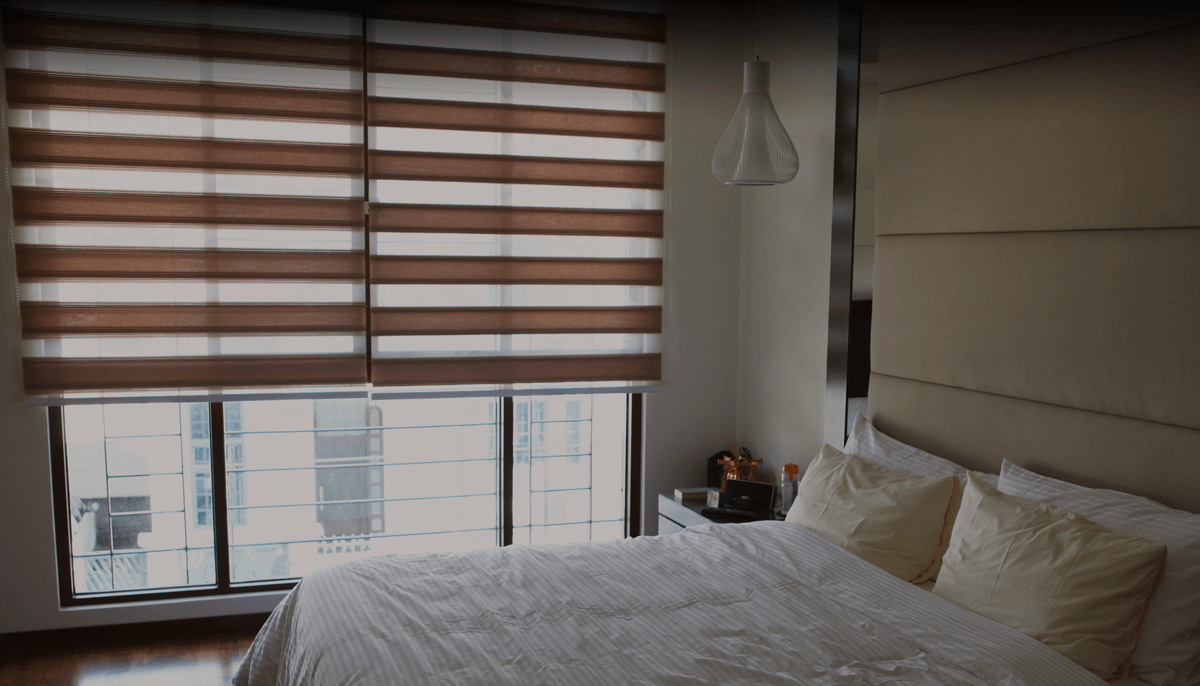 Modern bedroom with a neatly made bed and striped window blinds overlooking a city view