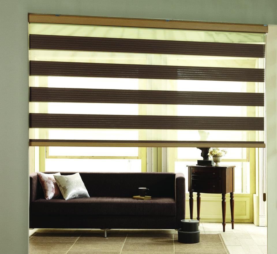Modern living room with striped window shades, dark sofa, and small side table near a bright window