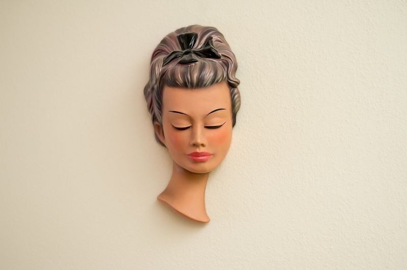 Eine Statue eines Frauenkopfes mit geschlossenen Augen auf einer weißen Wand.