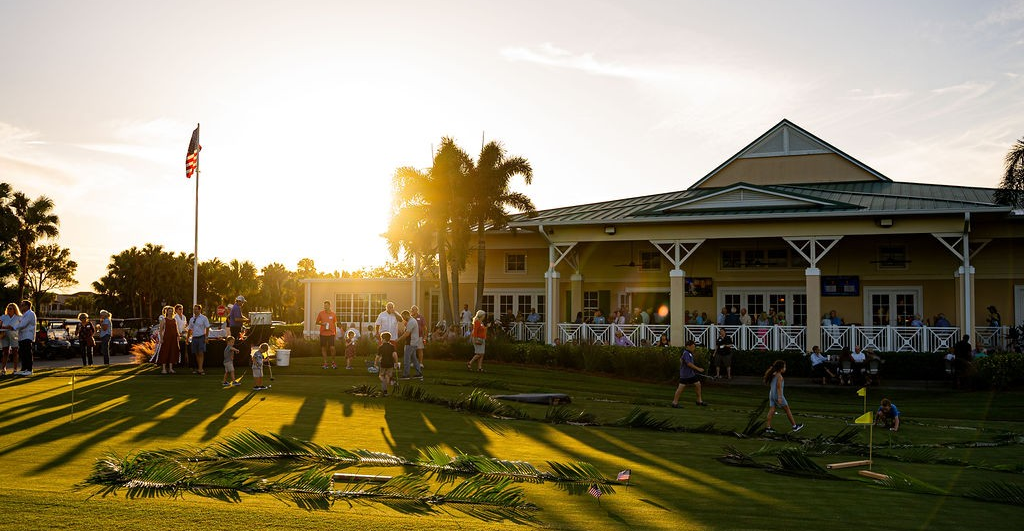 People gathered on a lawn in front of a yellow building at sunset.