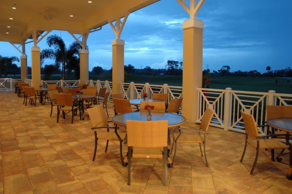Outdoor dining area with tables and chairs under a covered patio, overlooking a golf course at dusk.