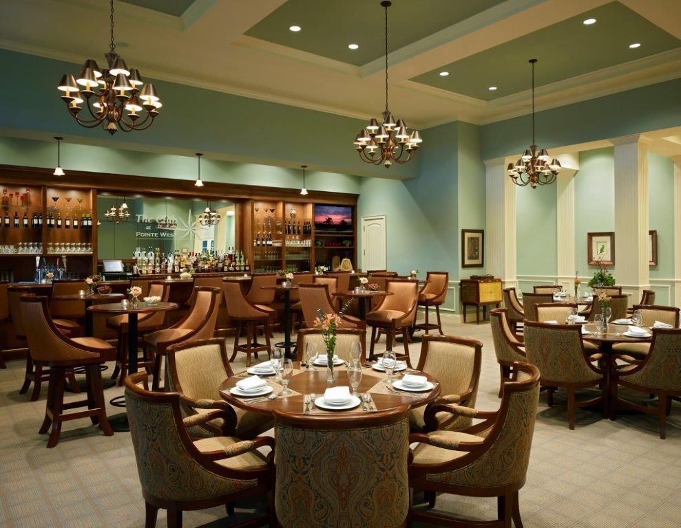 Restaurant interior with round tables, chairs, bar, chandeliers, and teal walls.