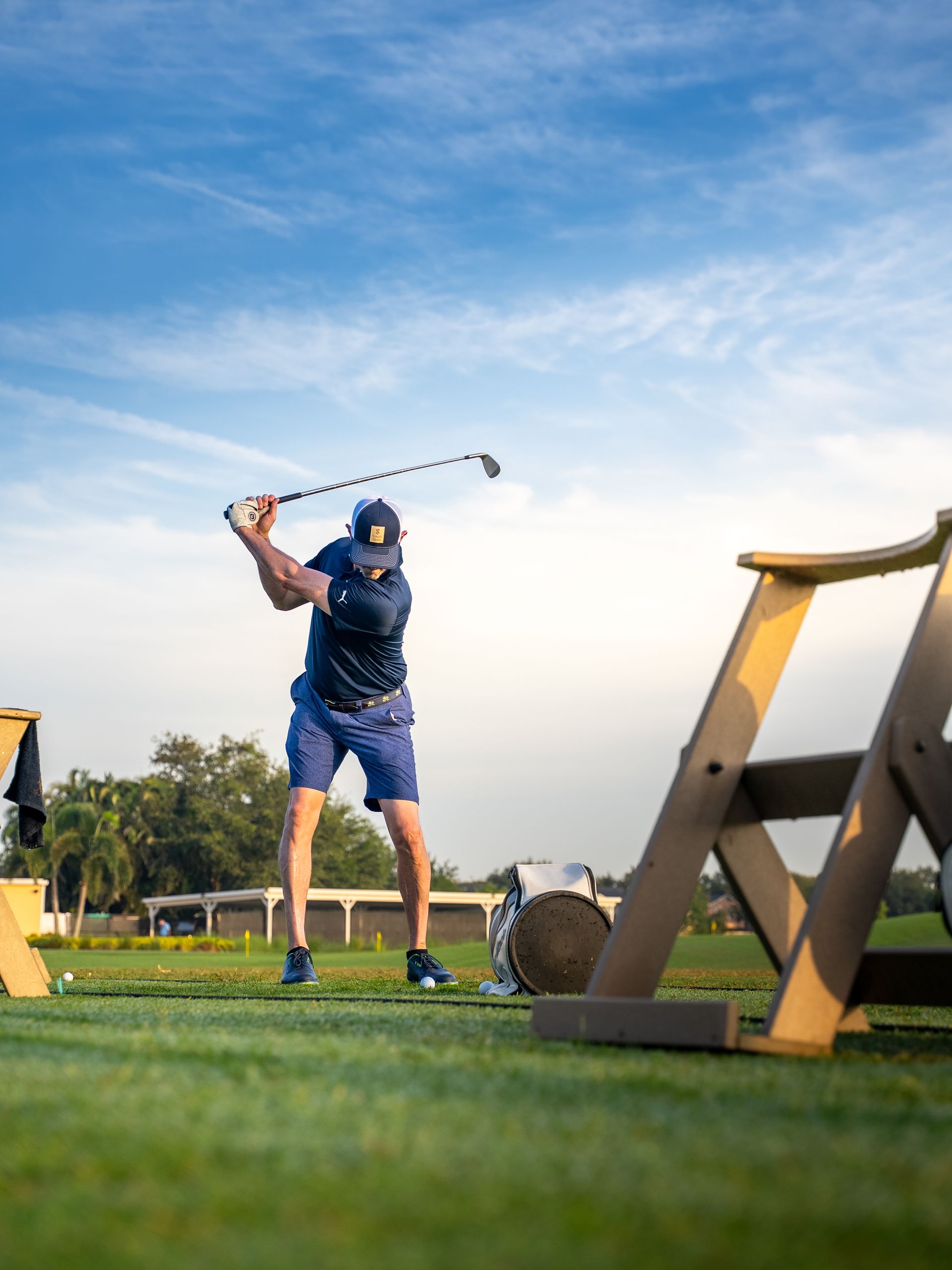 Golfer swings club on green; blue sky backdrop.