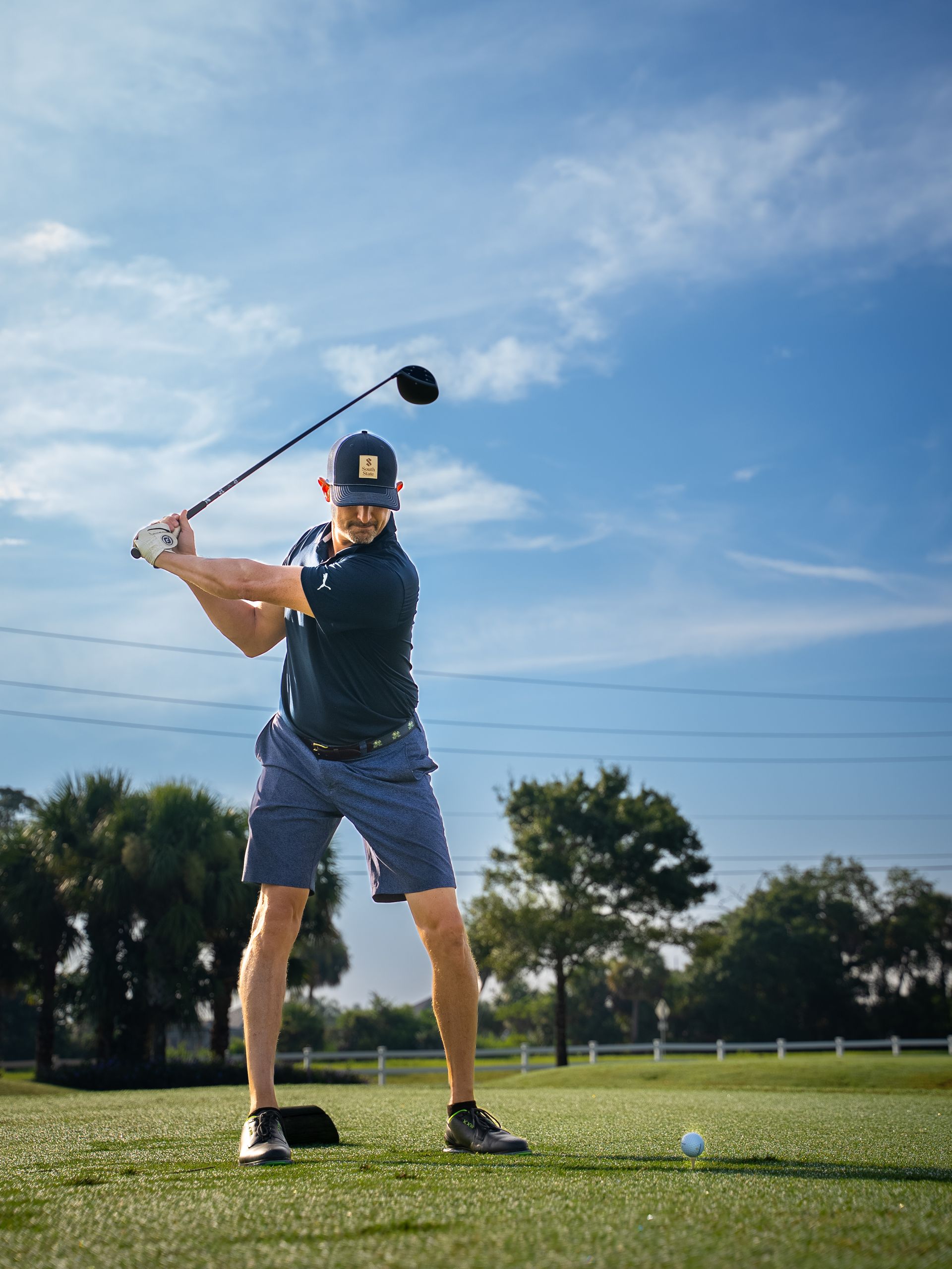 Golfer swings driver on green under blue sky.