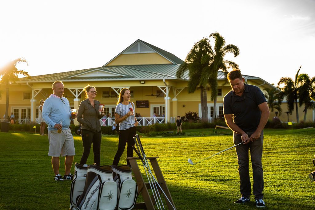 Man about to hit golf ball with others watching on a green, sunny day.
