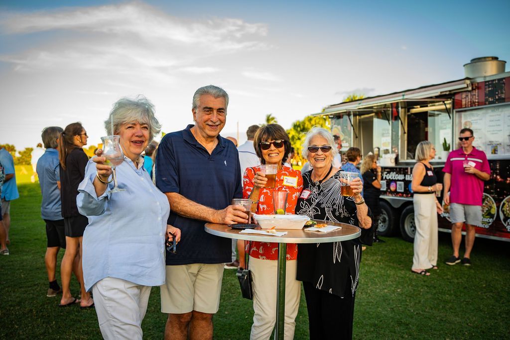 Group of people at an outdoor gathering, toasting with drinks near a food truck.