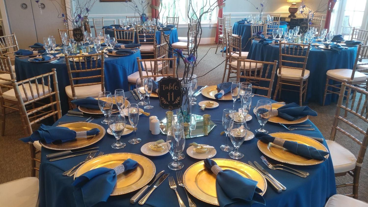 Elegant event tables set with gold chargers, blue linens, and centerpieces.