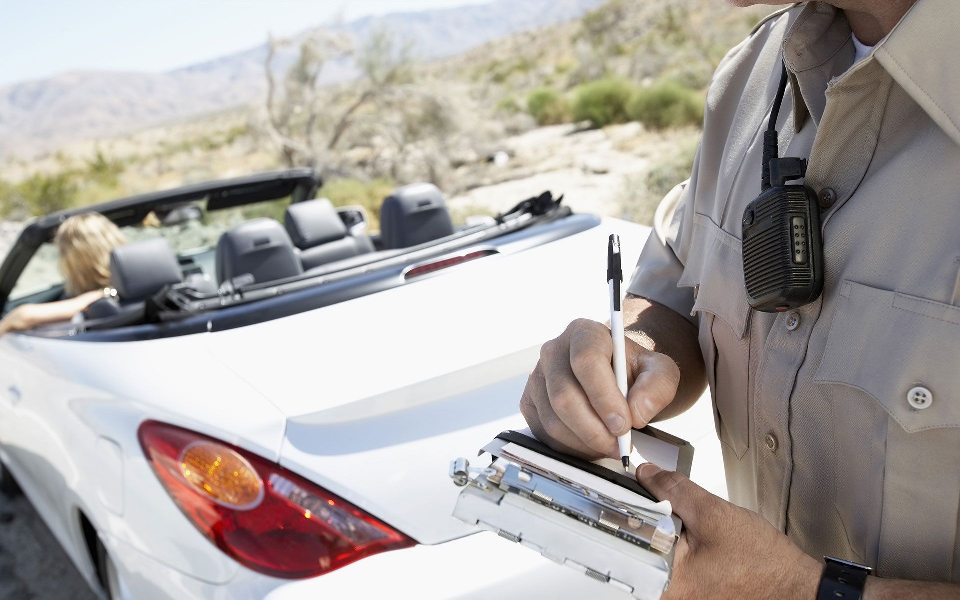 A police officer is writing a ticket in front of a white convertible car.