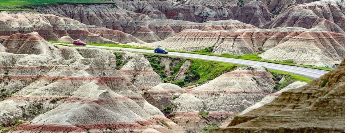 A car is driving down a road in the badlands.