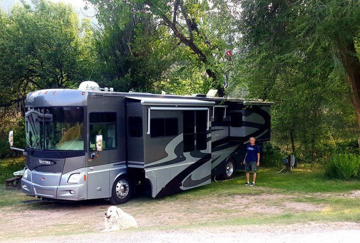 A man is standing next to a large rv parked in a grassy area.
