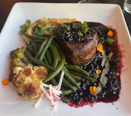 Plate of steak with blueberry sauce, green beans, cauliflower, mashed potatoes, and flowers.