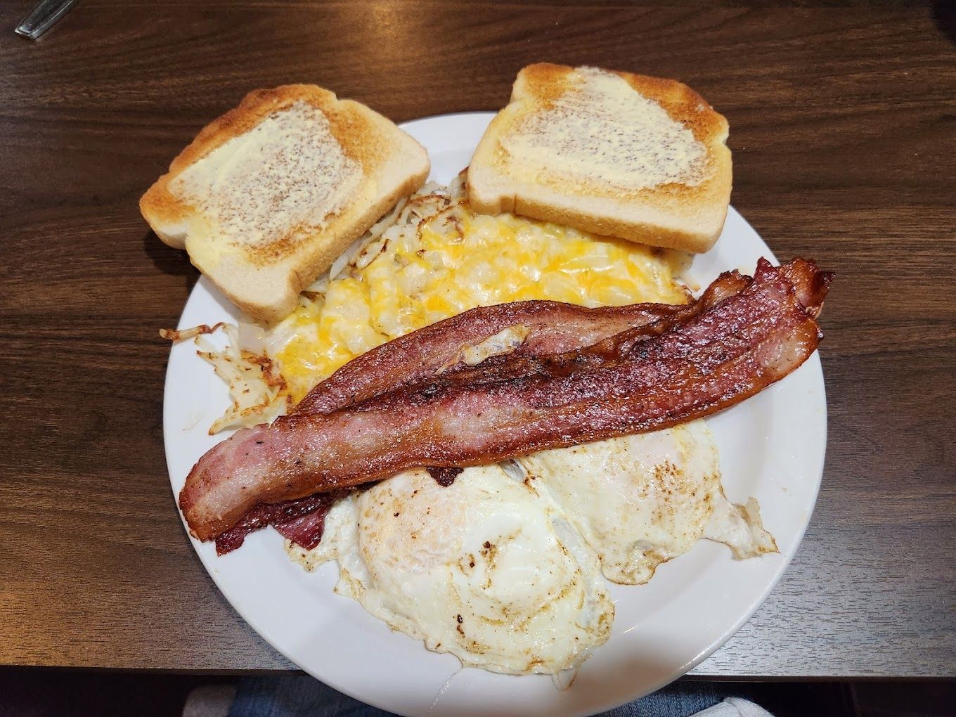 A white plate topped with eggs , bacon , and toast on a wooden table.