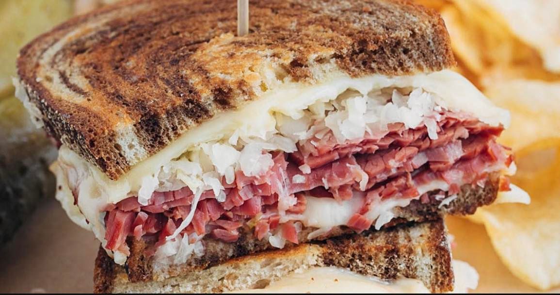A close up of a corned beef sandwich on a plate with chips.