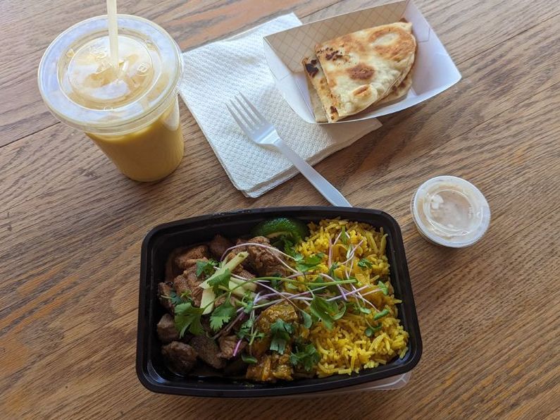 A container of food and a drink are on a wooden table.