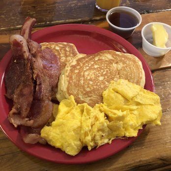 A red plate topped with pancakes , eggs and bacon on a wooden table.