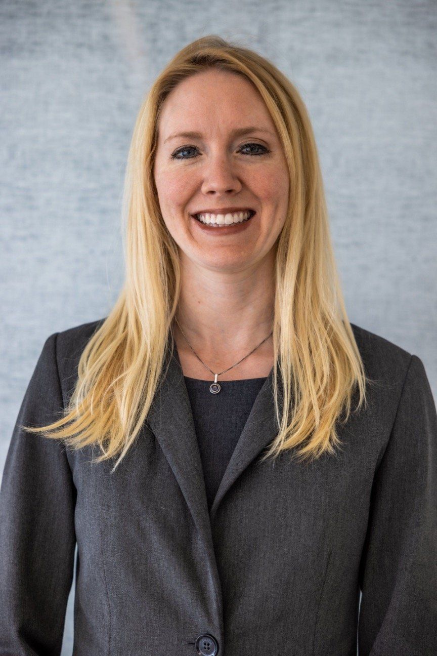 A woman in a suit and necklace is smiling for the camera.