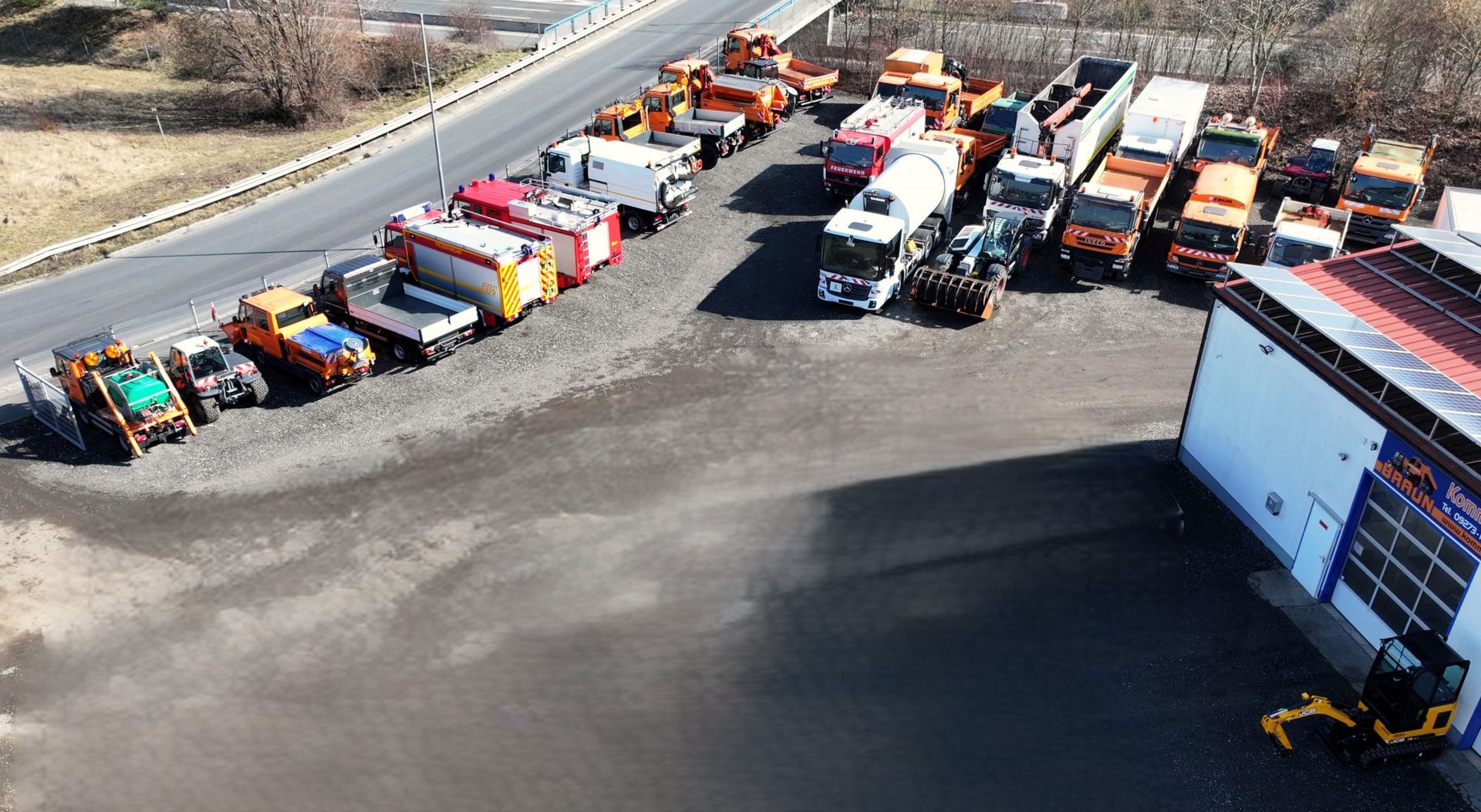 A row of trucks are parked in a parking lot next to a road.