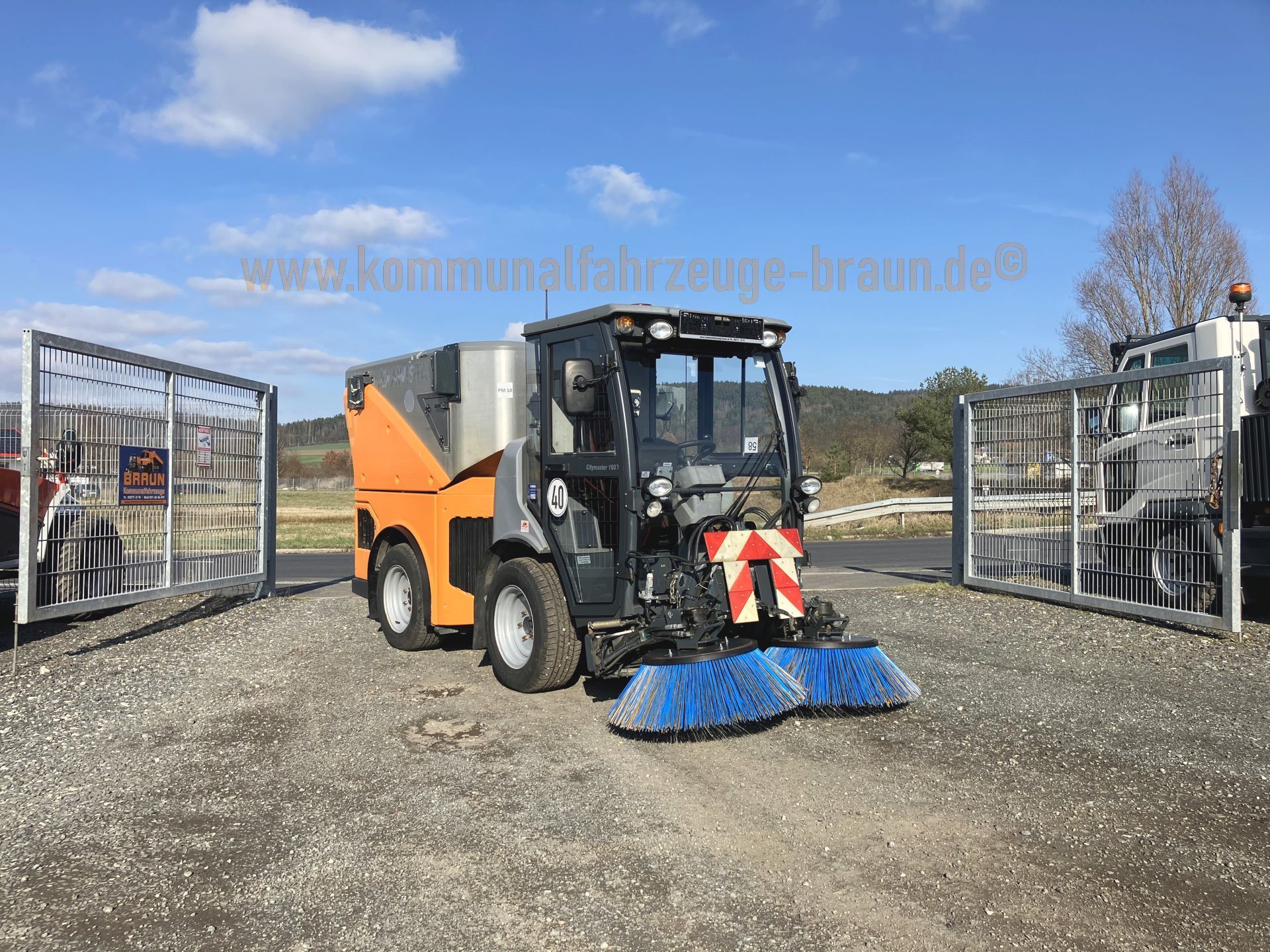 A street sweeper is parked in a gravel lot next to a fence.
