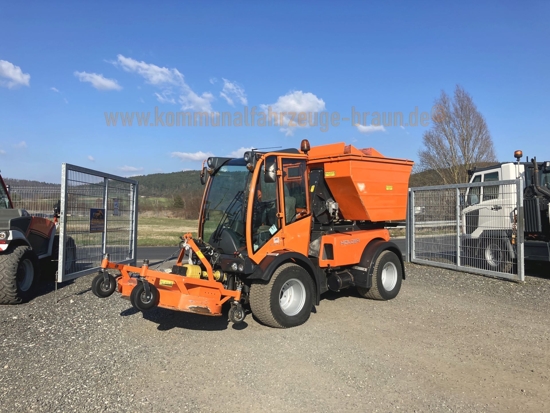 An orange tractor is parked in a gravel lot next to a fence.