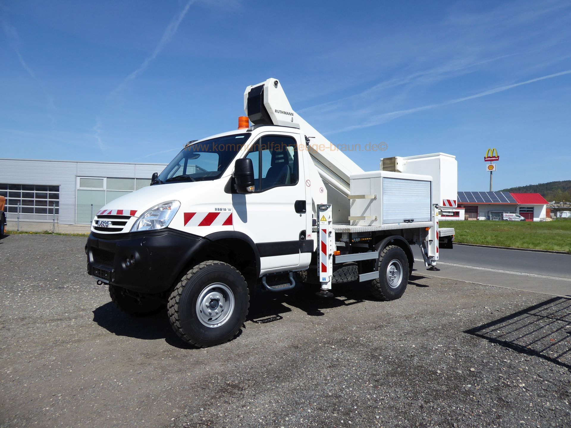A white truck with a crane on top of it is parked in a parking lot.