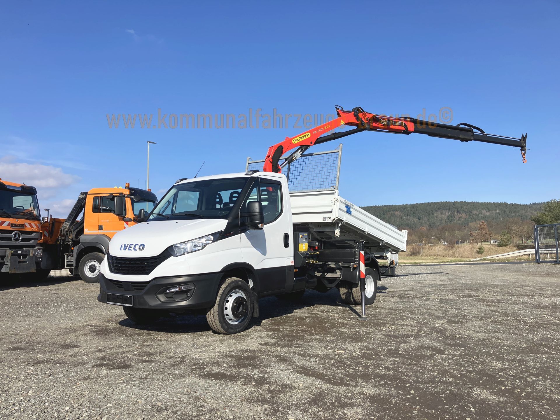 A white truck with a crane attached to it is parked in a gravel lot.