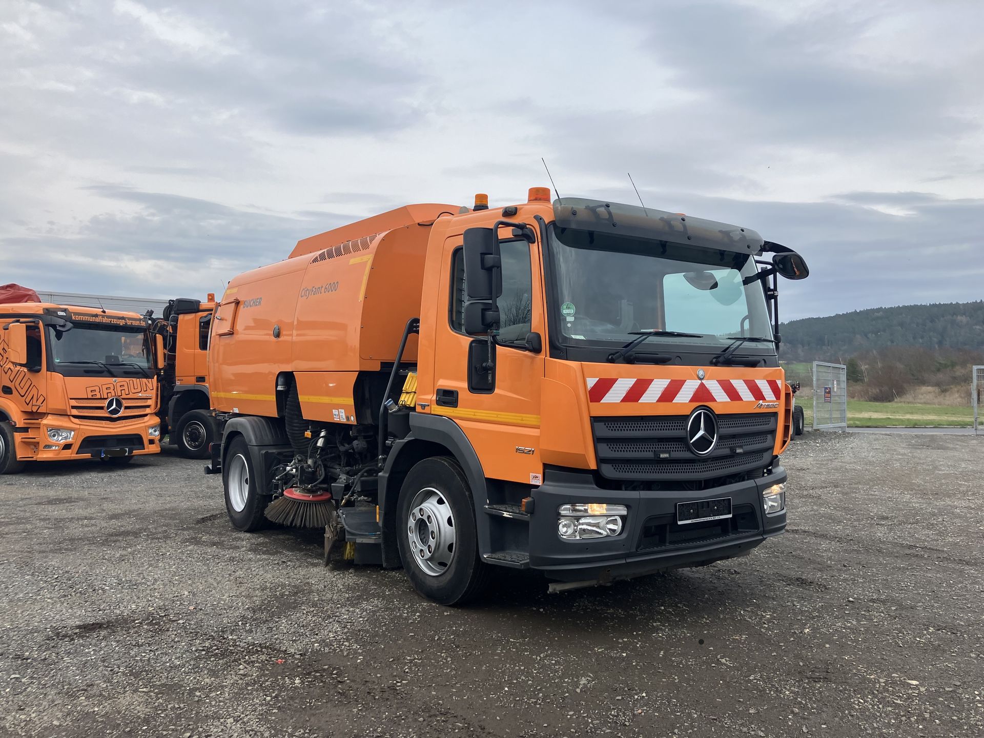 A mercedes benz street sweeper truck is parked in a gravel lot.