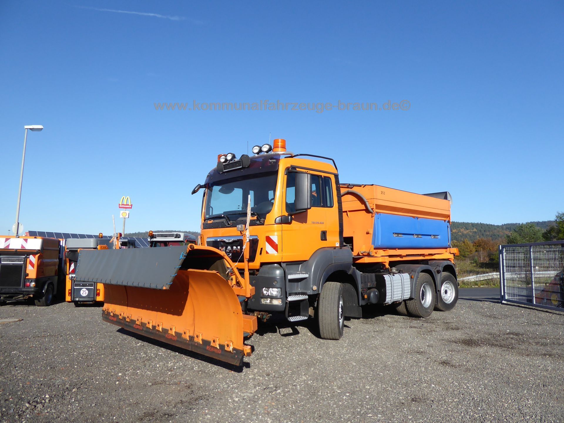 An orange truck with a snow plow attached to it is parked in a parking lot.