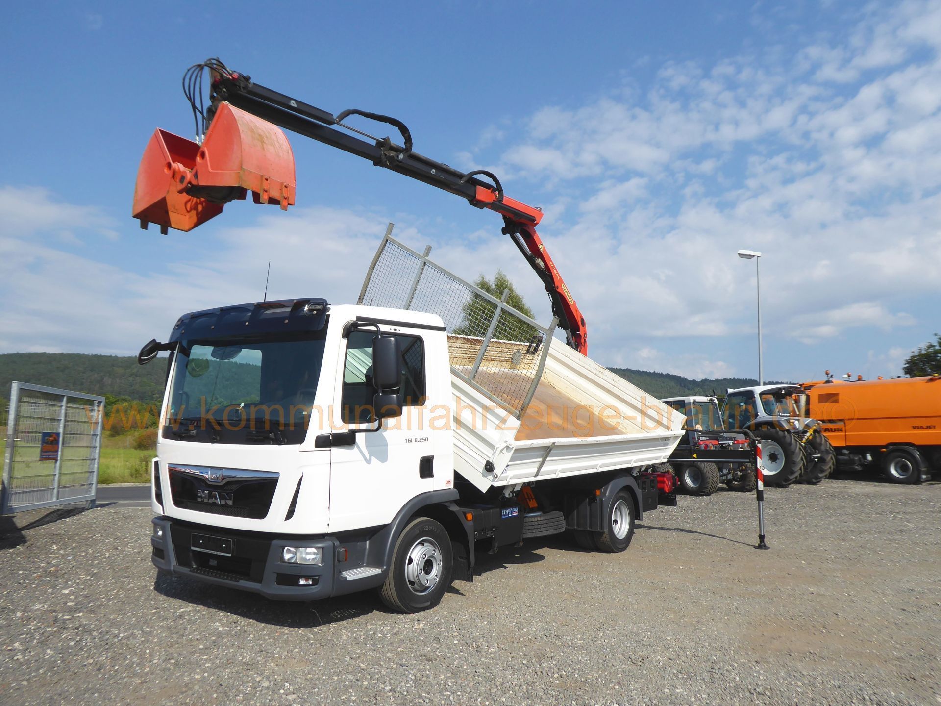 A dump truck with a crane attached to it is parked in a gravel lot.