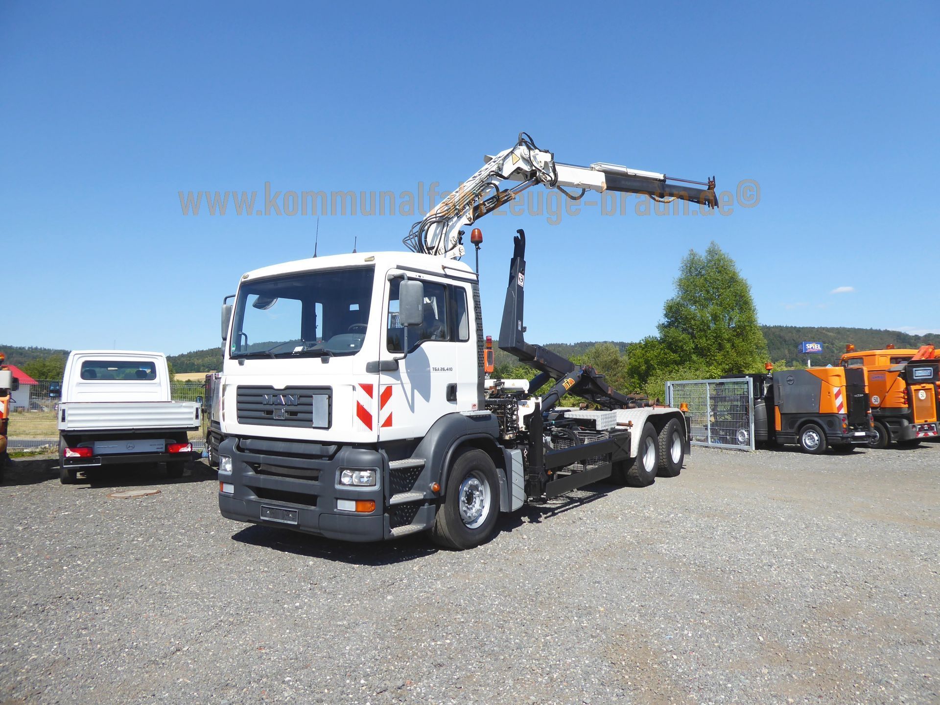 A man truck with a crane on the back is parked in a gravel lot