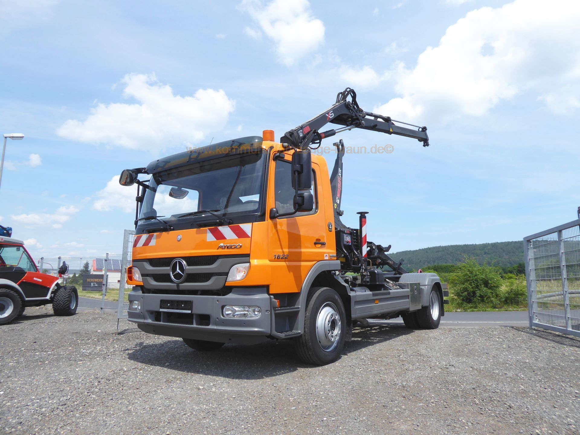 An orange truck with a crane on the back is parked in a gravel lot.