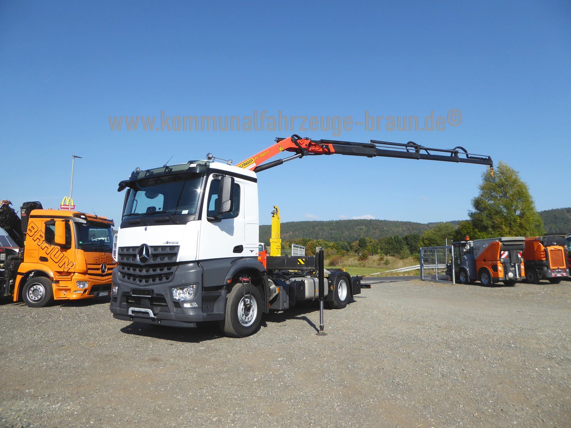 A truck with a crane attached to it is parked in a gravel lot.