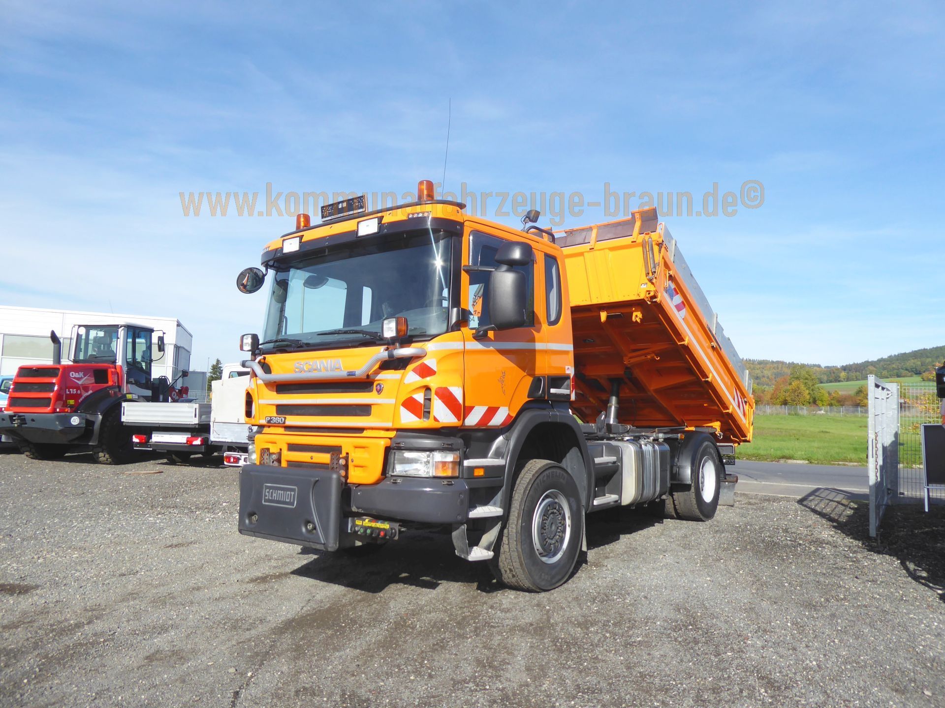 An orange dump truck is parked in a gravel lot