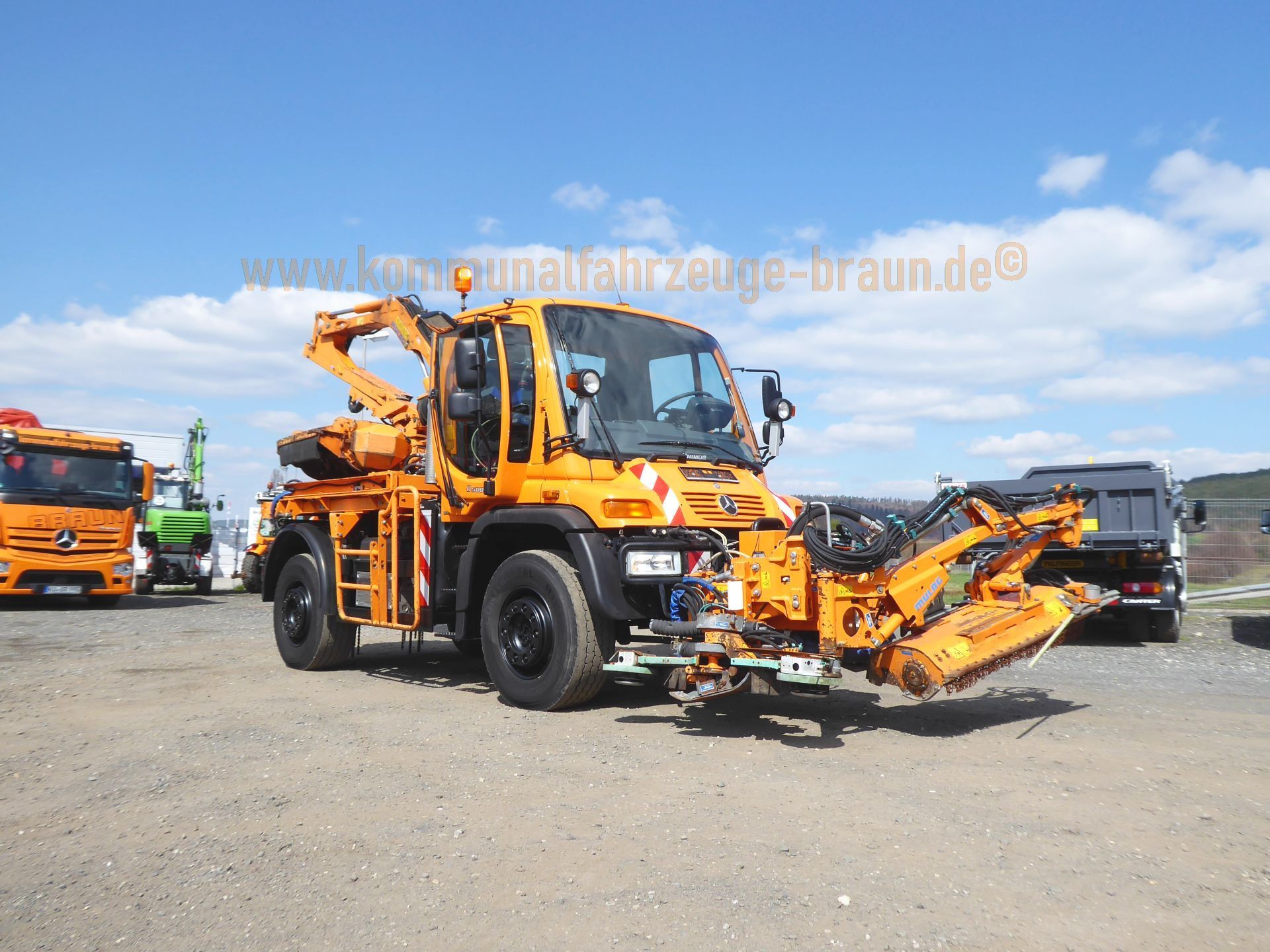 An orange truck is parked in a dirt lot