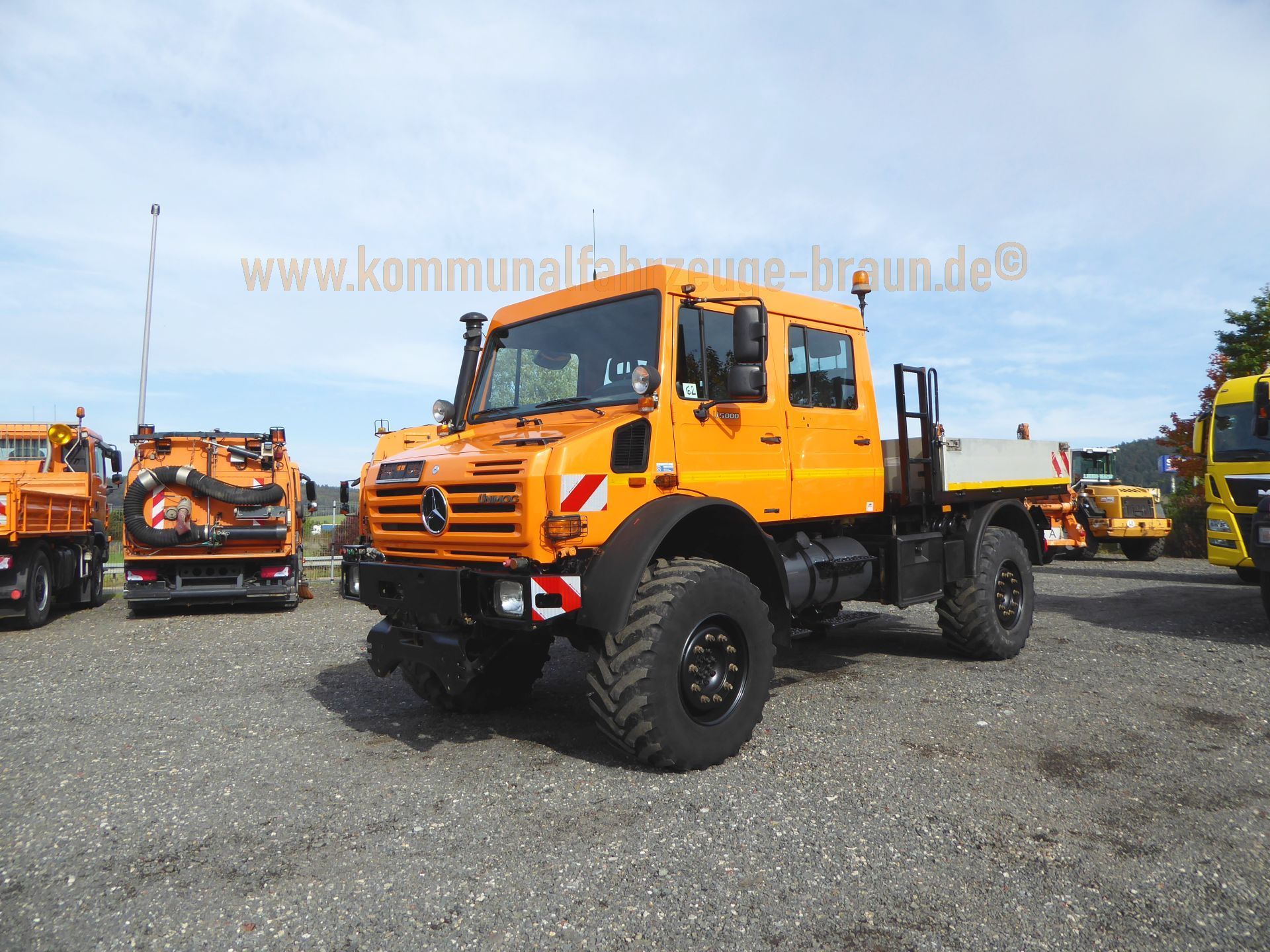 An orange truck is parked in a gravel lot next to other trucks.