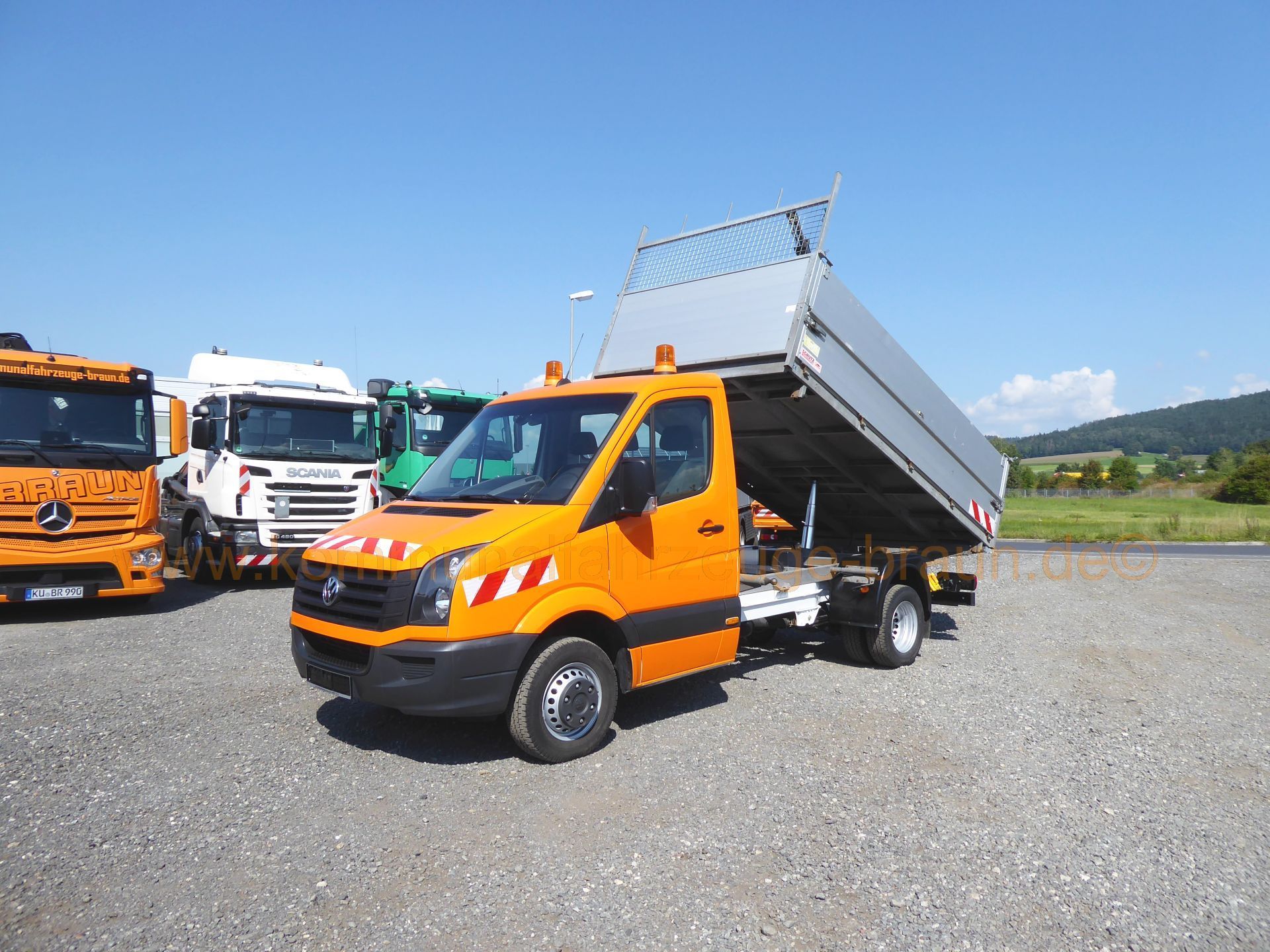 An orange dump truck is parked in a gravel lot next to other trucks.