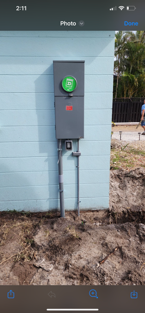 Gray electrical box mounted on a light blue wall, with conduit running into the ground.